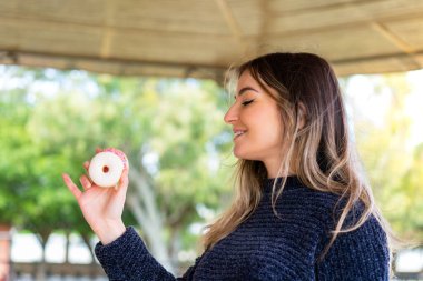 Genç, güzel Romen bir kadın açık havada yüzünde mutlu bir ifadeyle donut tutuyor.