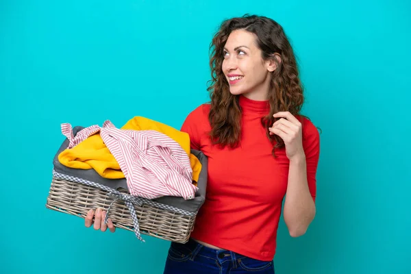 stock image Young caucasian woman holding a clothes basket isolated on blue background looking up while smiling