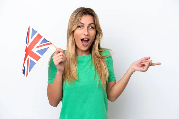 举着英国国旗 背景为白色的乌拉圭年轻女子感到惊讶 并指了指侧面 — 图库照片