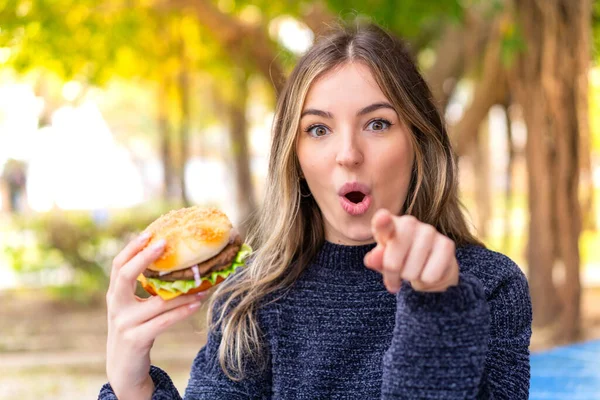 Młoda Ładna Rumuńska Kobieta Trzyma Hamburgera Świeżym Powietrzu Zaskoczony Wskazując — Zdjęcie stockowe