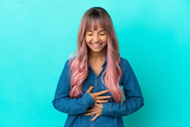 Mavi arka planda izole edilmiş pembe saçlı, melez bir kadın. Gülümsüyor.