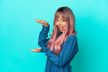 Mavi arka planda izole edilmiş pembe saçlı melez bir kadın ilan vermek için kopyalama alanı tutuyor.