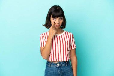 Mavi arka planda izole edilmiş genç melez kadın bir şey gösteriyor.