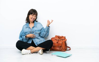 Genç bir bayan, beyaz arka planda tek başına oturmuş gitar hareketi yapıyor.