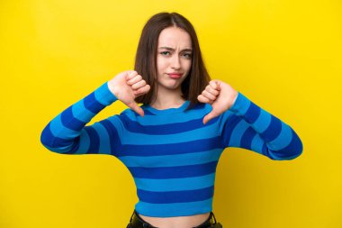 Sarı arka planda izole edilmiş genç Ukraynalı kadın baş parmağını iki eliyle aşağı gösteriyor.