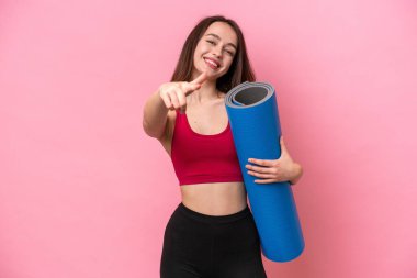 Genç sporcu Ukraynalı kadın yoga derslerine giderken elinde pembe arka planda izole edilmiş bir minder tutarken mutlu bir ifadeyle ön tarafı işaret ediyor.