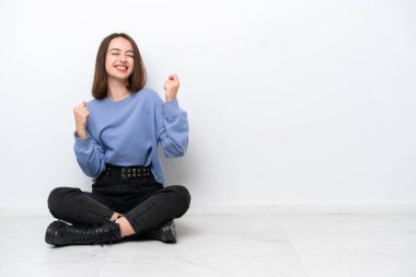 Young Ukrainian woman sitting on the floor isolated on white background celebrating a victory