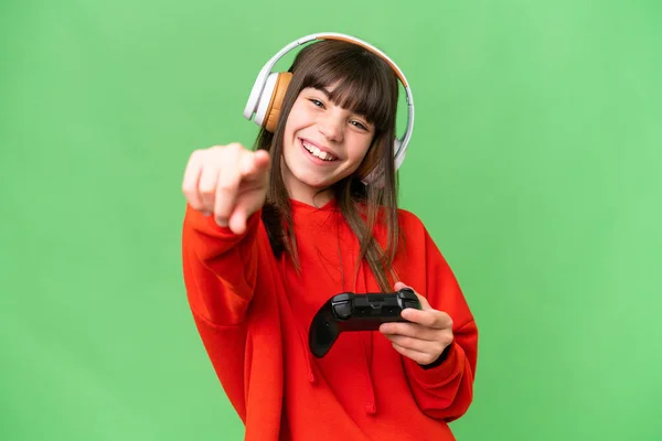 一个小高加索女孩在一个孤立的背景下玩电子游戏控制器 带着快乐的表情指着前面 — 图库照片