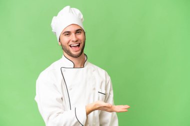 Genç, yakışıklı aşçı, izole edilmiş arka planda bir fikir sunuyor ve gülümsüyor.