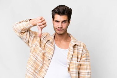 İzole edilmiş beyaz arka planda genç, yakışıklı beyaz bir adam, olumsuz bir ifadeyle baş parmağını aşağı gösteriyor.