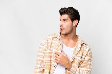 Beyaz arka plan üzerinde genç, yakışıklı beyaz bir adam. Yan tarafa bakarken sürpriz jest yapıyor.