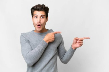 Soyutlanmış beyaz arka planı olan yakışıklı beyaz bir adam şaşırmış ve işaret ediyor.