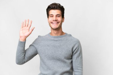 Young handsome caucasian man over isolated white background saluting with hand with happy expression