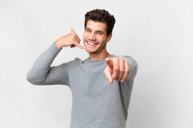 Beyaz arka planda yaşayan yakışıklı beyaz bir adam telefon jesti yapıyor ve ön tarafı işaret ediyor.