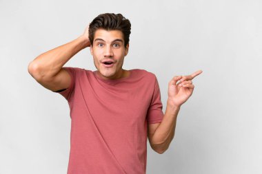 Young handsome caucasian man over isolated white background surprised and pointing finger to the side
