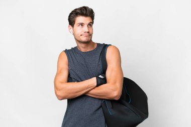 Spor çantalı beyaz tenli genç beyaz adam omuzlarını kaldırırken şüpheyle hareket ediyor.