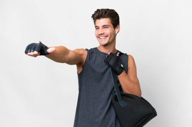 Spor çantalı, beyaz arka planda beyaz tenli genç beyaz bir adam baş parmak hareketi yapıyor.