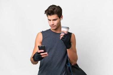 Young sport caucasian man with sport bag over isolated white background holding coffee to take away and a mobile