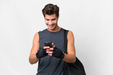 Spor çantalı beyaz tenli genç beyaz adam cep telefonuyla bir mesaj gönderiyor.