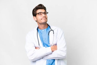 Genç doktor, izole edilmiş beyaz arka plan üzerinde omuzlarını kaldırırken şüphe jestleri yapıyor.