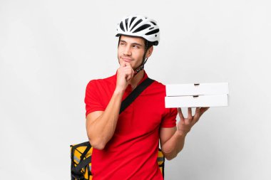 Pizza delivery man with work uniform picking up pizza boxes over isolated white background and looking up