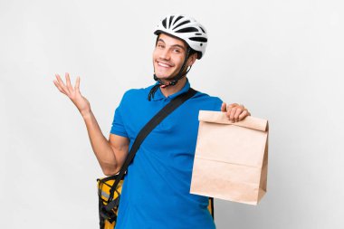 Kafkasyalı genç bir adam, izole bir arka plandan bir paket yiyecek alıyor ve gelmesi için ellerini yana uzatıyor.