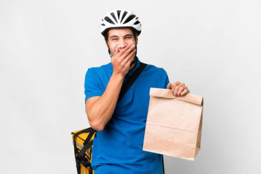 Kafkasyalı genç bir adam izole edilmiş arka planda bir paket yiyecek alıyor mutlu ve ağzı eliyle kaplayarak gülümsüyor.