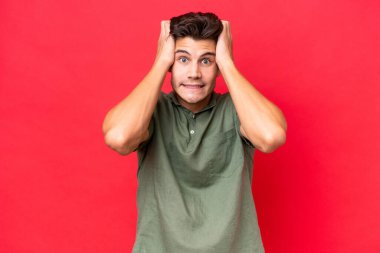 Kızıl arka planda izole edilmiş genç, beyaz, yakışıklı bir adam gergin hareketler yapıyor.