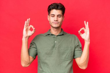 Zen pozisyonunda kırmızı arka planda izole edilmiş beyaz yakışıklı bir adam.