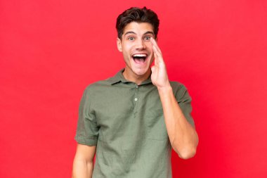 Kafkasyalı yakışıklı adam kırmızı arka planda izole edilmiş, şaşırmış ve şok olmuş bir yüz ifadesi var.