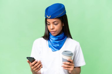 Uçak hostesi Afrikalı Amerikalı bir kadın izole edilmiş arka planda kahve ve bir cep telefonu tutuyor.