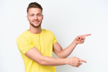 Beyaz arka planda izole edilmiş genç, sarışın, beyaz bir adam parmak göstererek bir ürün sunuyor.