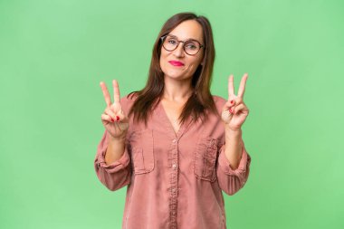 Orta yaşlı beyaz kadın izole edilmiş geçmişinde zafer işaretini iki elle gösteriyor.