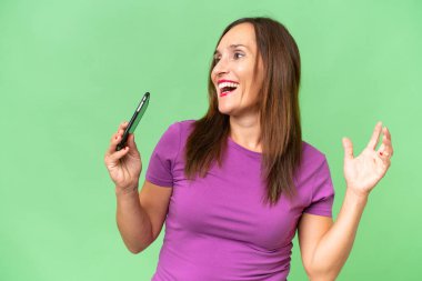 Orta yaşlı beyaz kadın izole edilmiş arka planda cep telefonu kullanıyor ve şarkı söylüyor.