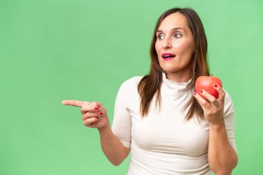 Stüdyonun arka planında elma tutan orta yaşlı kadın. 