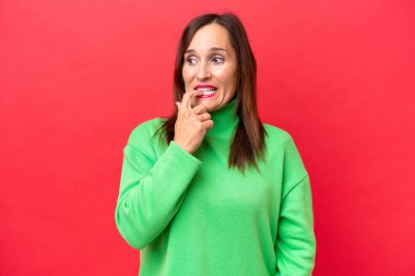 Orta yaşlı beyaz kadın, kırmızı arka planda izole edilmiş, gergin ve korkmuş.