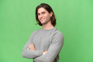 Genç beyaz adam yeşil krom arka planda izole edilmiş, kolları bağlı ve ileriye bakıyor.