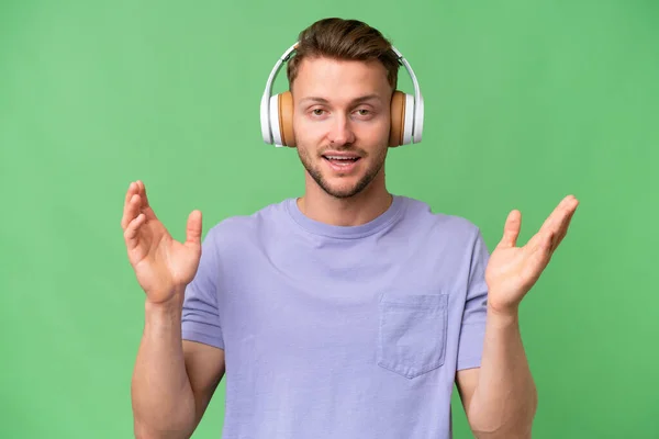 Jonge Blonde Kaukasische Man Geïsoleerde Achtergrond Verrast Luisteren Muziek — Stockfoto