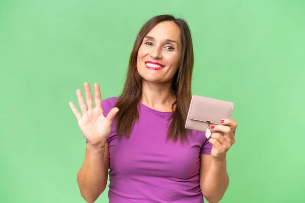 中年の白人女性は 幸せな表情で手で塩漬け孤立した背景の上に財布を持っています — ストック写真