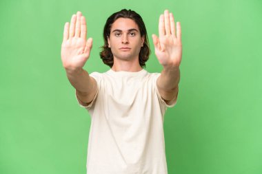 Yeşil krom arka planda izole edilmiş genç beyaz adam dur hareketi yapıyor ve hayal kırıklığına uğruyor.