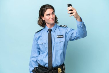 Genç polis, mavi arka planda izole edilmiş beyaz bir adam selfie çekiyor.