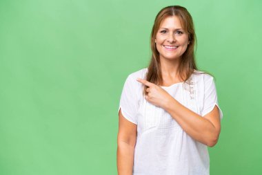 İzole edilmiş geçmişi olan orta yaşlı beyaz bir kadın bir ürünü sunmak için kenarı işaret ediyor.