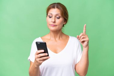 Orta yaşlı beyaz kadın izole edilmiş arka planda cep telefonu kullanıyor ve parmağını kaldırıyor.