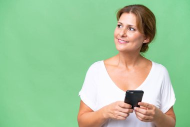 Orta yaşlı beyaz kadın izole edilmiş arka planda cep telefonu kullanıyor ve araştırıyor.