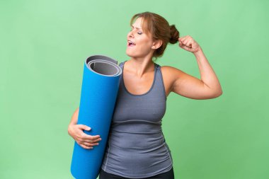 Orta yaşlı sporcu bir kadın yoga derslerine giderken izole bir arka planda bir minder tutarak zaferi kutluyor.