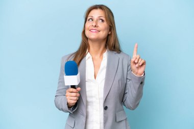 İzole edilmiş mavi arka planda orta yaşlı televizyon sunucusu kadın harika bir fikre işaret ediyor.