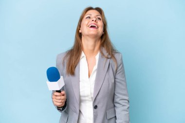 Orta yaşlı televizyon sunucusu kadın izole edilmiş mavi arka planda gülüyor.