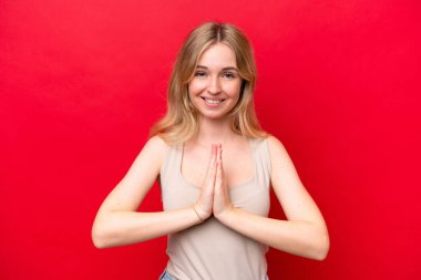 Kırmızı arka planda izole edilmiş genç İngiliz kadın avuç içlerini bir arada tutuyor. İnsan bir şey ister.