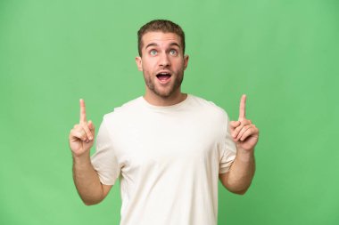 Yeşil krom arka planda izole edilmiş yakışıklı beyaz adam şaşırmış ve yukarı bakıyor.