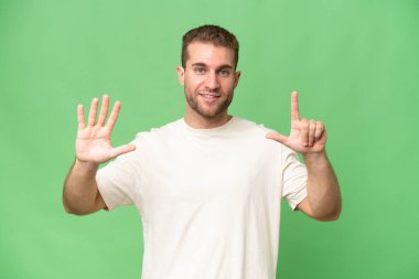 Yeşil krom arka planda tecrit edilmiş yakışıklı beyaz adam parmaklarıyla yediyi sayıyor.